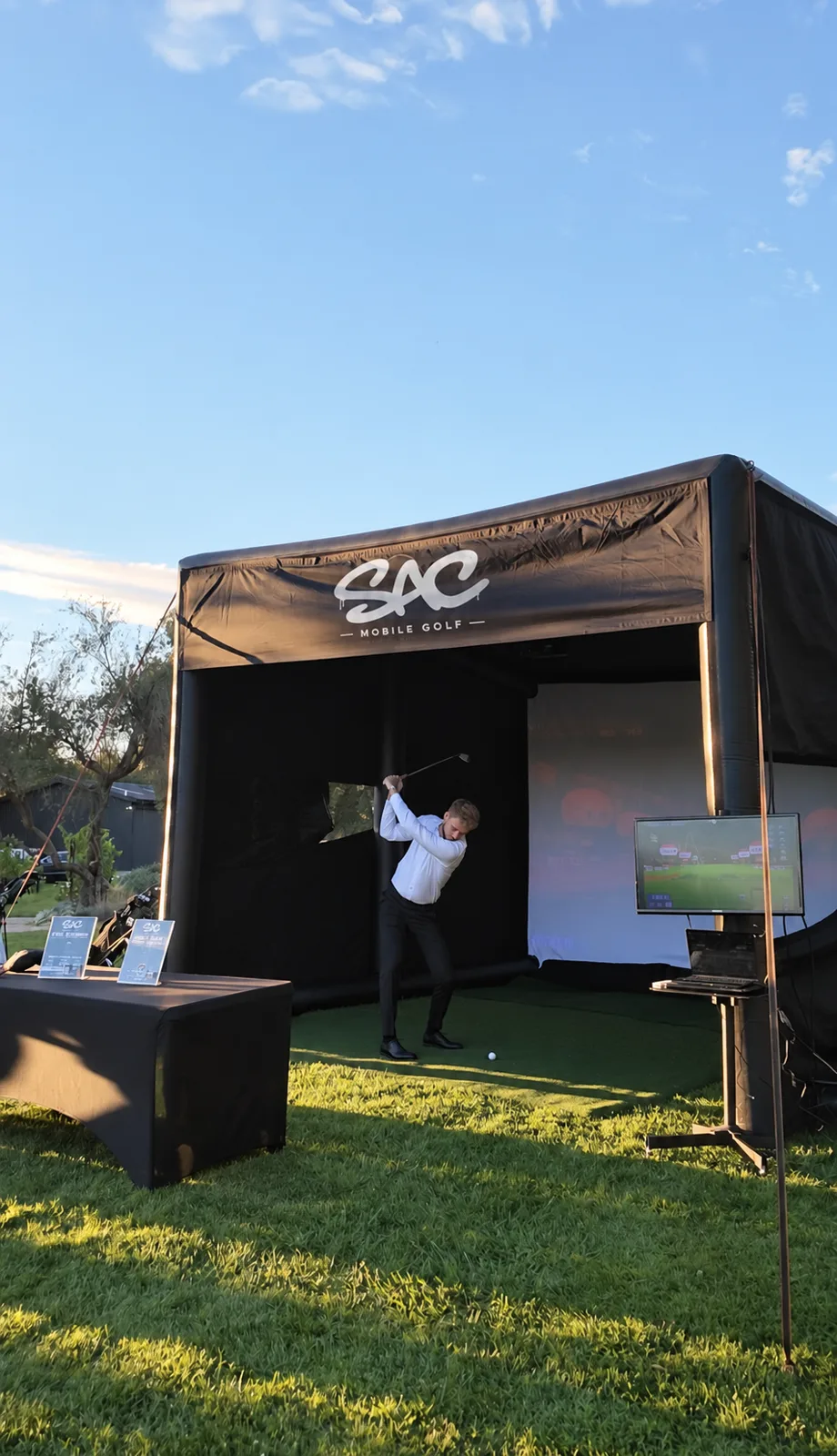 Golfer swinging inside the Sac Mobile Golf simulator tent on a sunny lawn